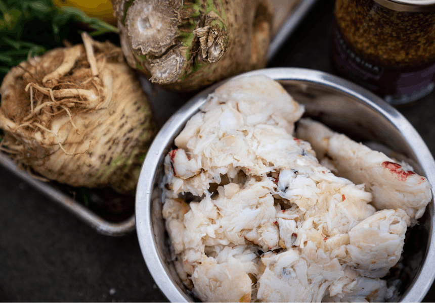 silver bowl full of crab meat, next to root vegetables and milled mustard
