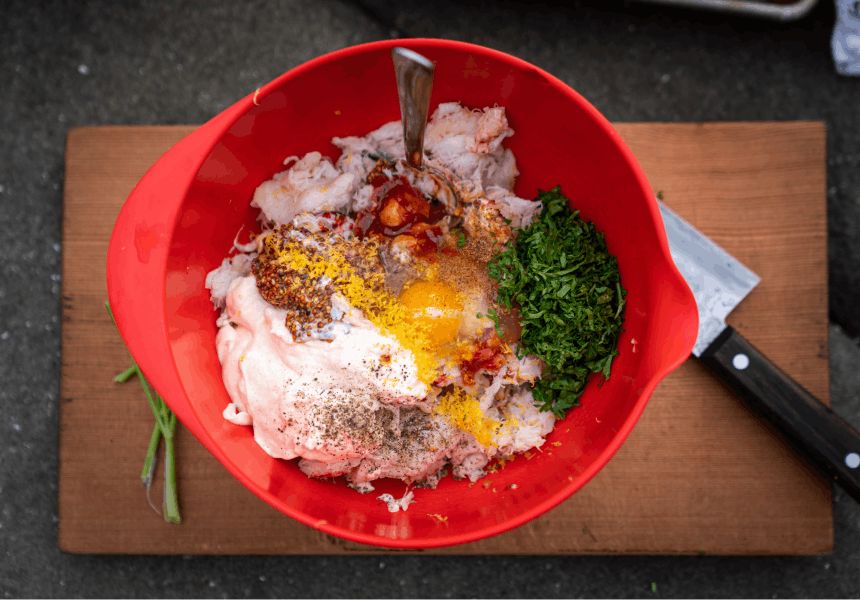crab meat, egg, mayonnaise and herbs in a red bowl sitting on top of a wooden board next to a knife