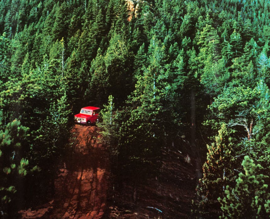 red bronco driving down a dirt road in the middle of a pine forest