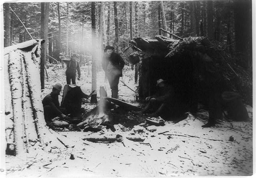 old black and white image of a group of people sitting around a fireplace in a snowy campsite in the forest