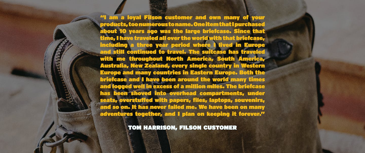 旅行と茶色のフィルソンブリーフケースバッグに重ねられたフィルソン商品の品質についてのトムハリソンからの長い引用