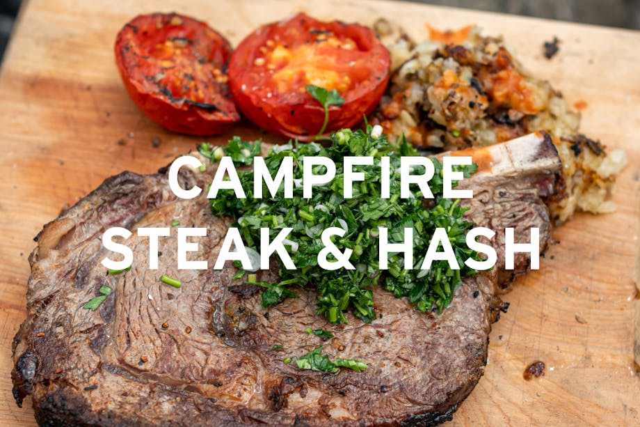 bone in steak with diced herbs, roasted halved tomato and potato hash on a wooden cutting board center text 