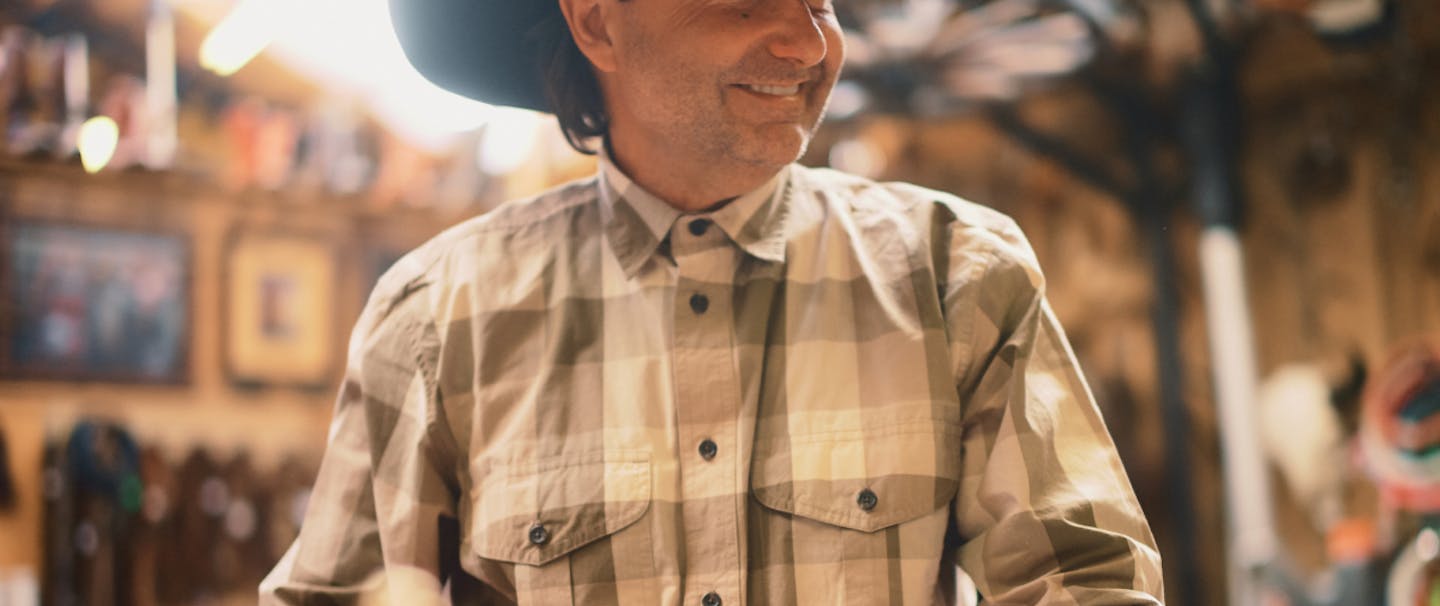 man in a dark cowboy hat wearing a white and brown shirt