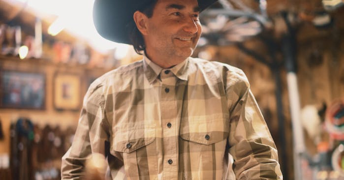 man in a dark cowboy hat wearing a white and brown shirt
