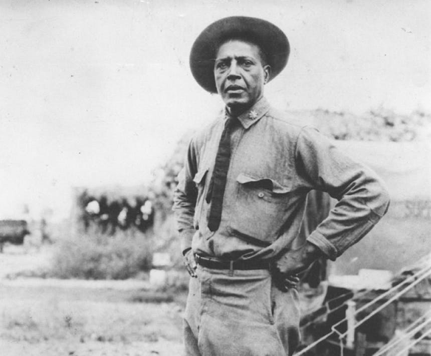 black and white image of person in park ranger shirt with thin black tie, standing in a field with a tent in the background