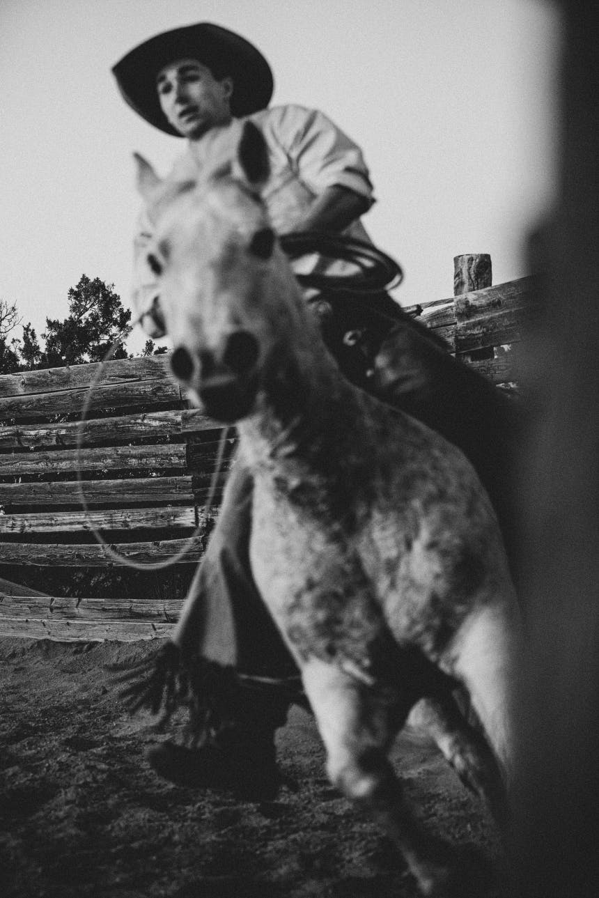 black and white image of dappled horse being ridden by a cowboy