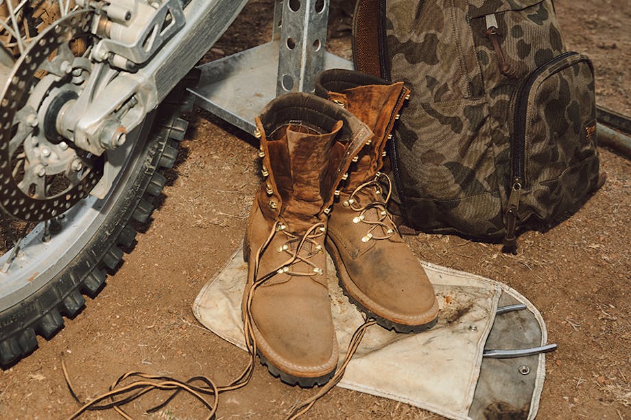 boots set on a white tool pouch next to a camouflage backpack and motorcycle