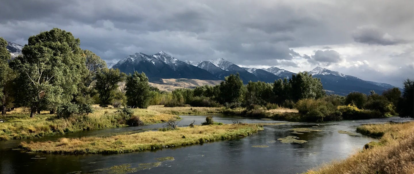 river meanders in foreground with bucolic meadow and snow capped mountains in background