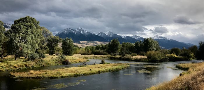 river meanders in foreground with bucolic meadow and snow capped mountains in background