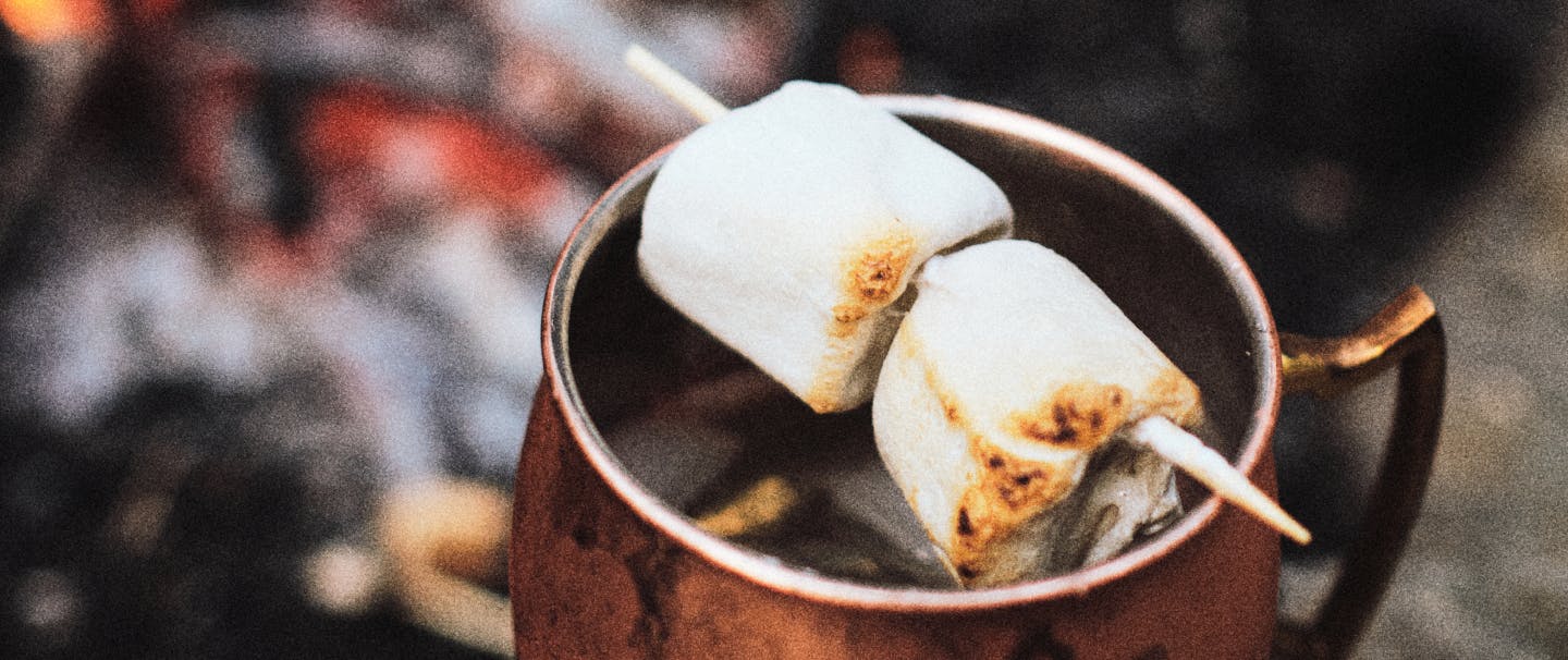 melted marshmallows stuck through with a wood skewer balanced over the lip of a copper mug