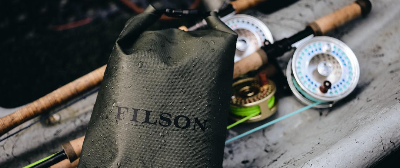 small filson dry bag next to two fly fishing rods on a surface in a boat