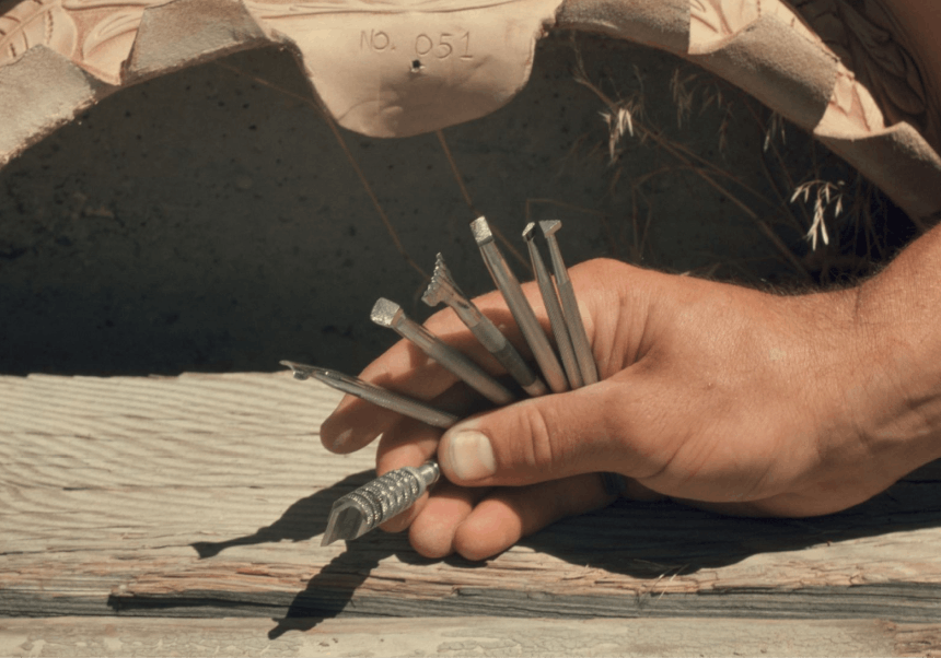 hands holding various silver metal tools used for hand tooling leather