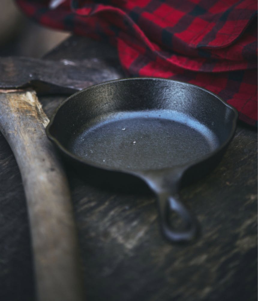 a cast iron skillet sitting next to an axe and a red and black plaid shirt
