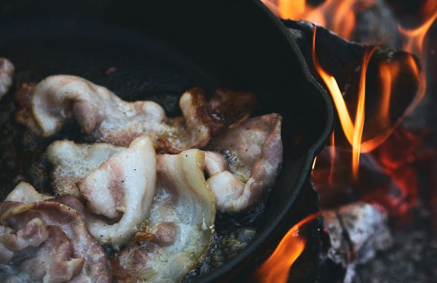 bacon cooking in a cast iron skillet over a fire