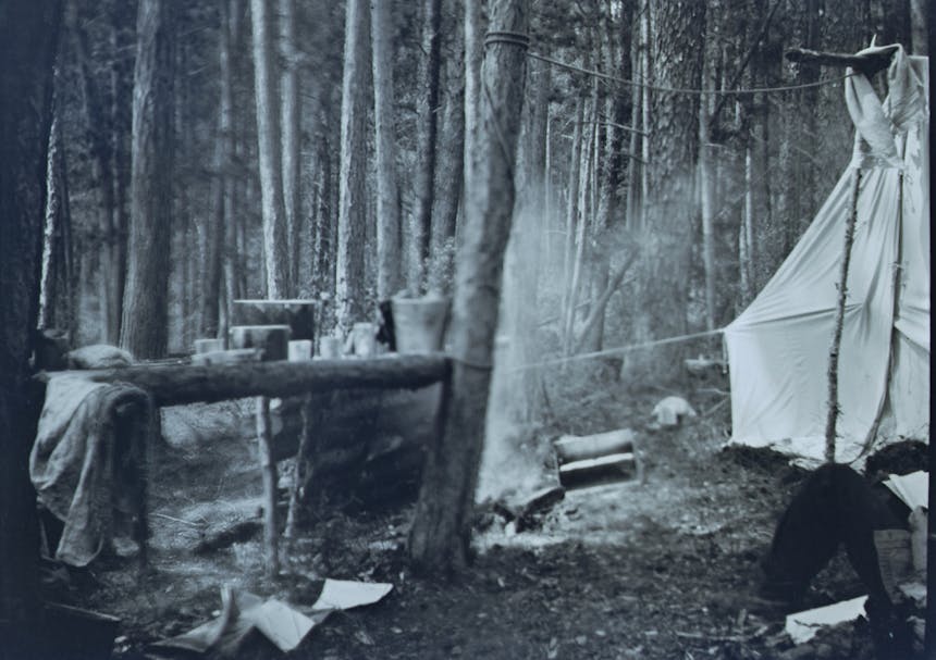 black and white image of a campsite with a large white tent and kitchen implements and firepit next to the tent