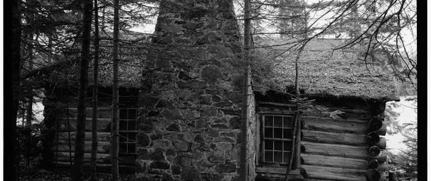 black and white image of a log cabin with a large central stone chimney