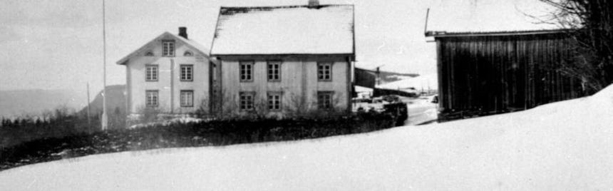 black and white image of two old white washed house structures and a dark barn in a snowy field