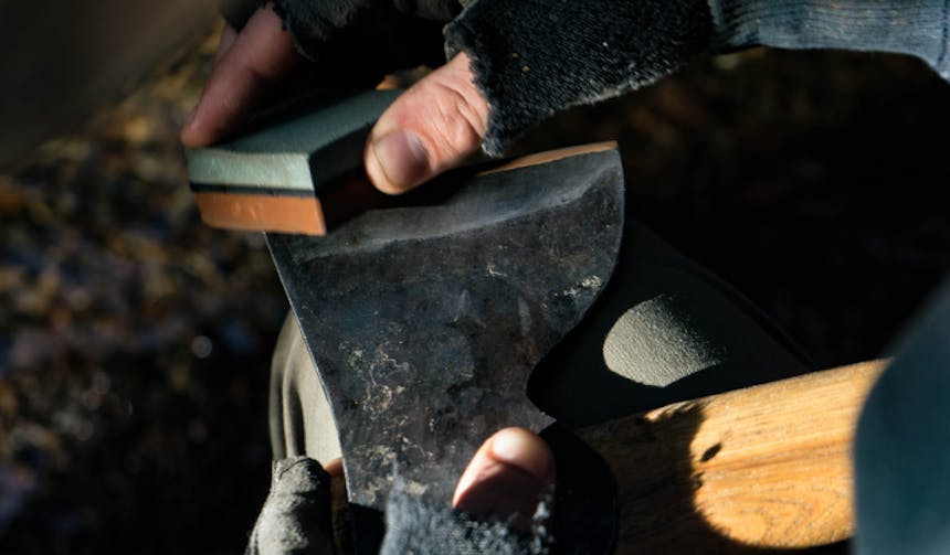 hand using a whet stone to hone an axe