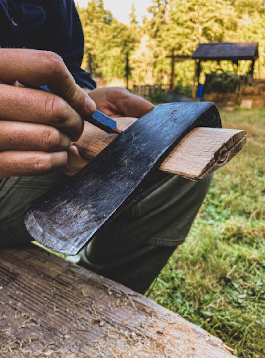 person drawing on an axe handle underneath the axe head in a grassy meadow