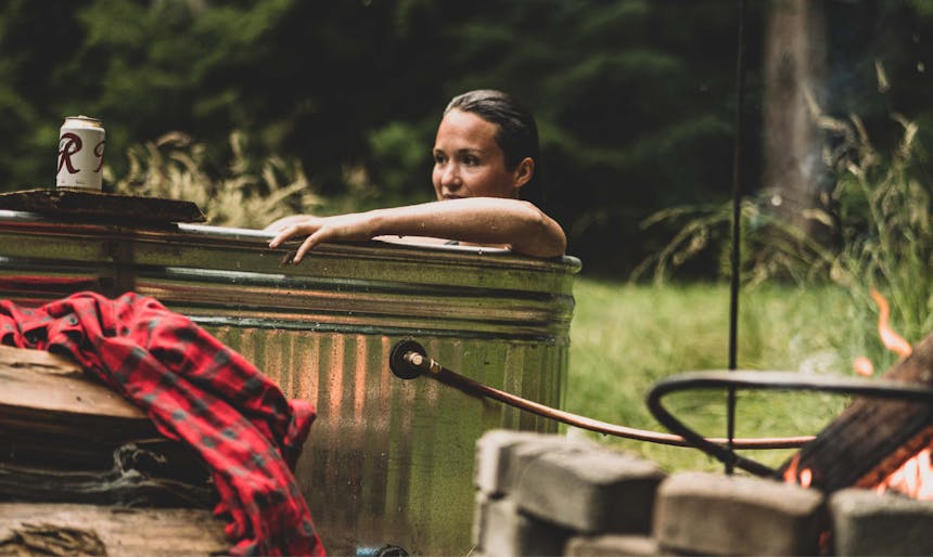 woman sitting in a homemade aluminum hottub in a meadow