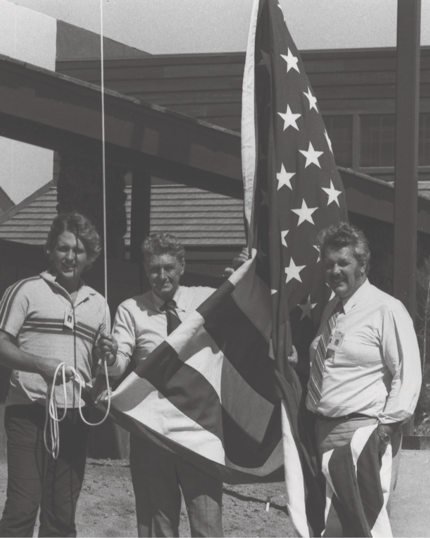 three people in a yard holding the american flag tied up on a flag pole