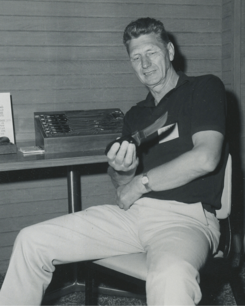 man in khaki pants sitting on a chair holding a fixed blade knife