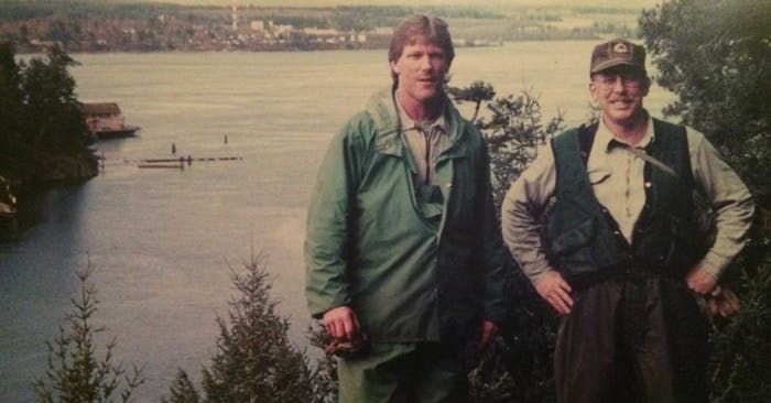 two men standing in the woods overlooking a large body of water