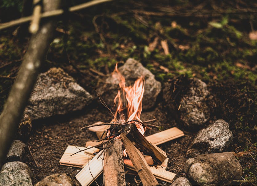 a tent style campfire burning in a firepit outside