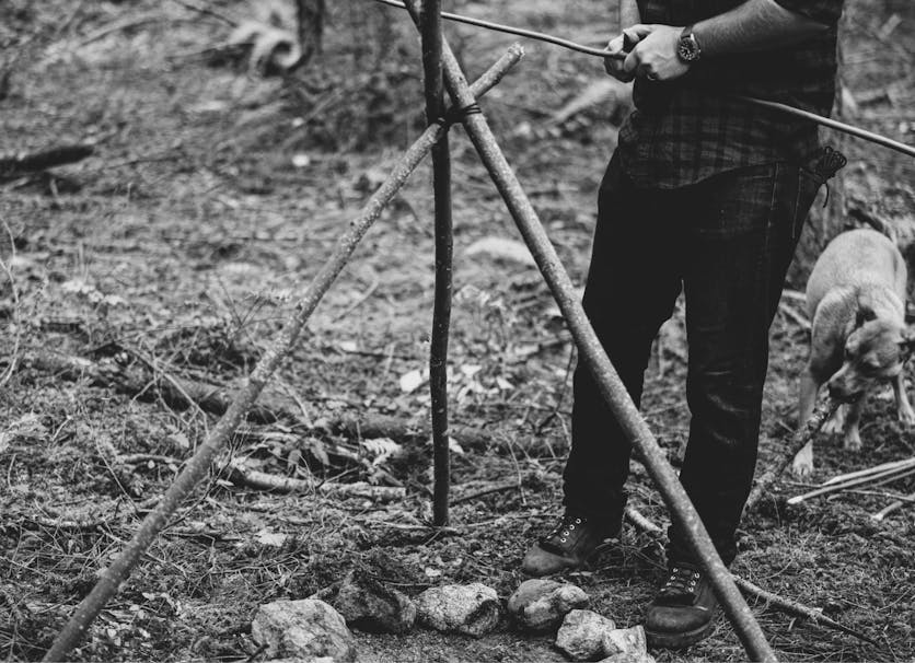 person setting up a cooking rig with three sticks for use over a fire