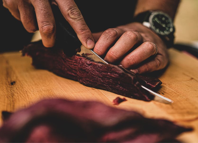 hands using a knife to cut along the grain of a large cut of venison