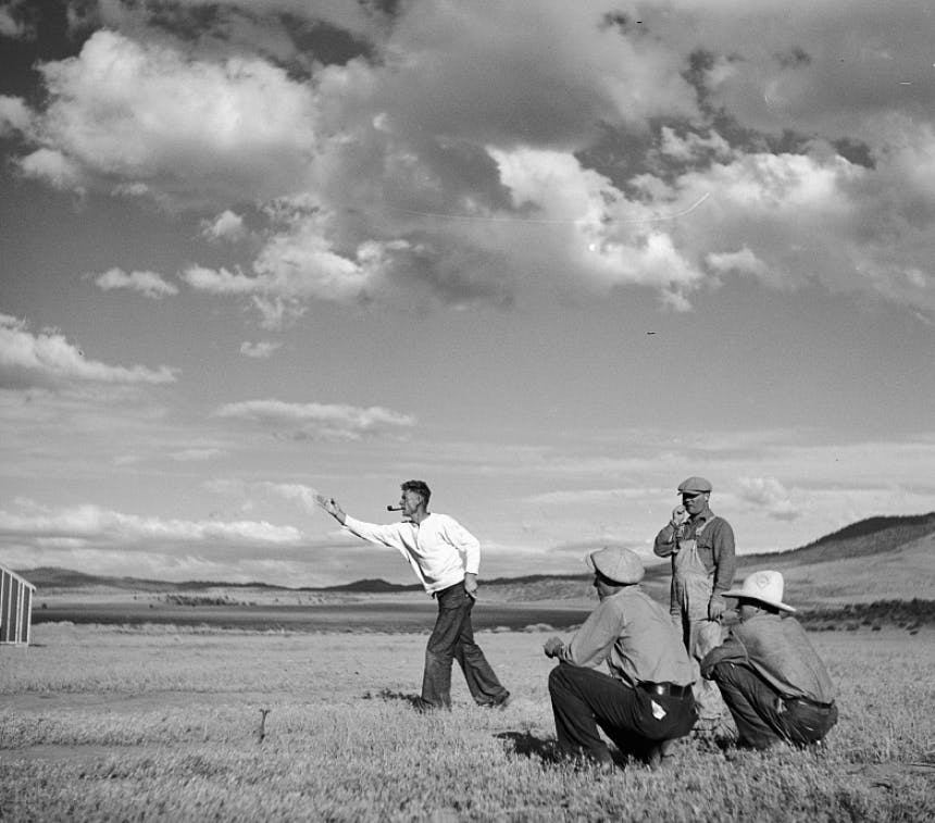 men in a field throwing horseshoes wearing antiquated clothes