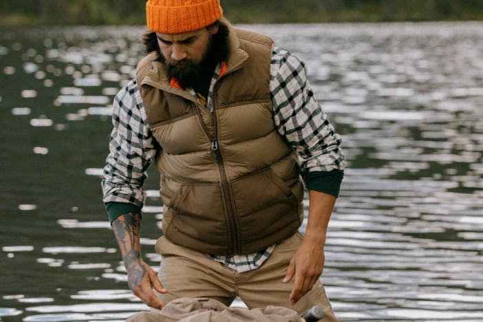 person in white and green plaid brown vest and orange hat standing in front of a lake