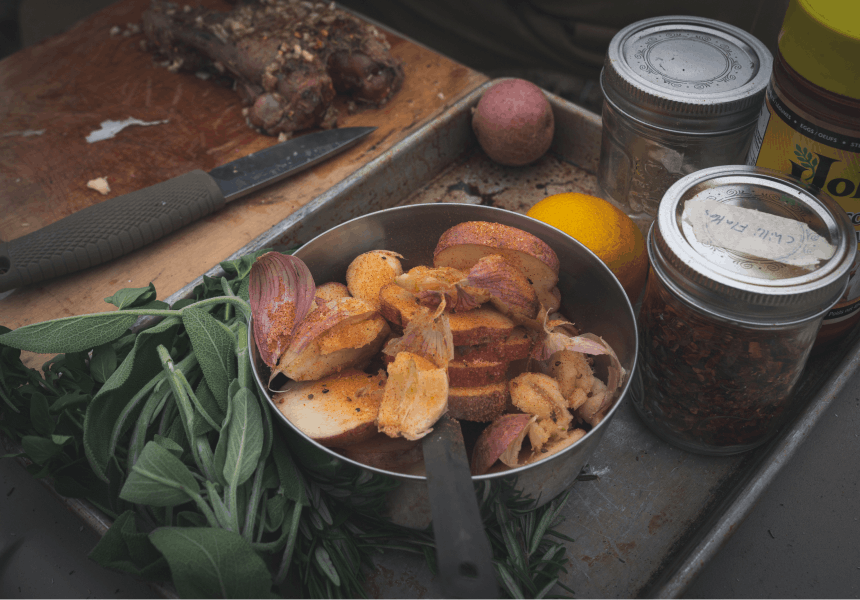 vegetables in a metal pot next to herbs and spices on a baking sheet