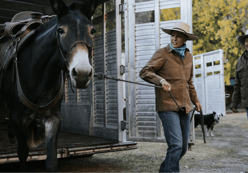 woman in tan hat and brown jacket leading a horse out of a livestock trailer