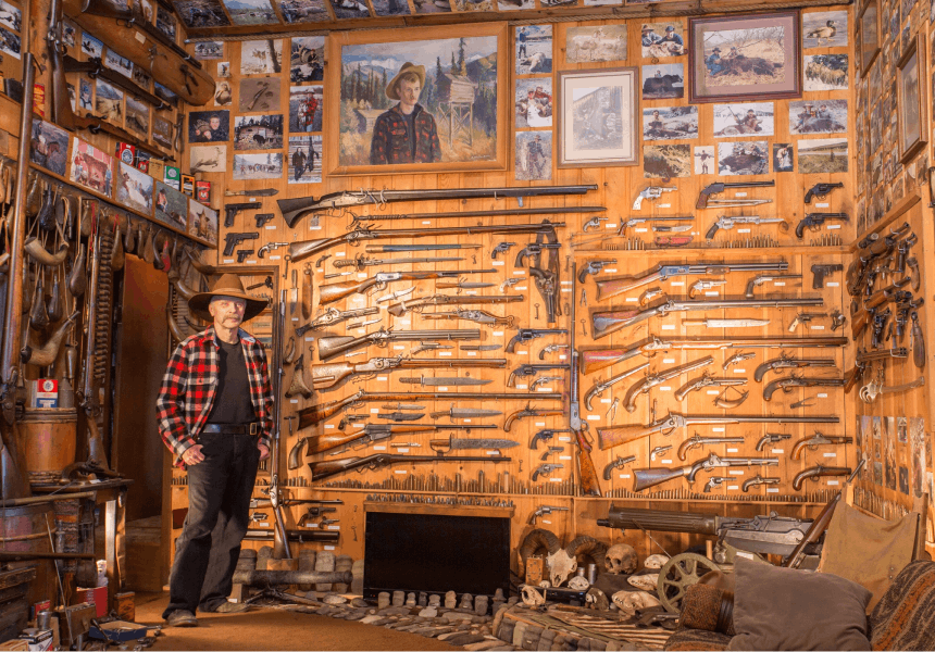 man standing in a room with a large number of mounted guns, knives, and paintings at the rainy pass lodge