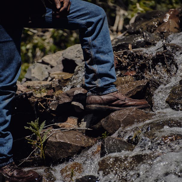 流れる水によって岩の上に立っているブーツカット洗浄ジーンズを着ている男