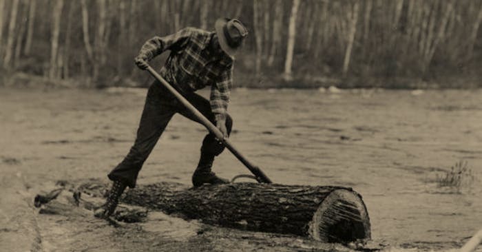 vintage sepia image of logger standing on log in river with logger tool