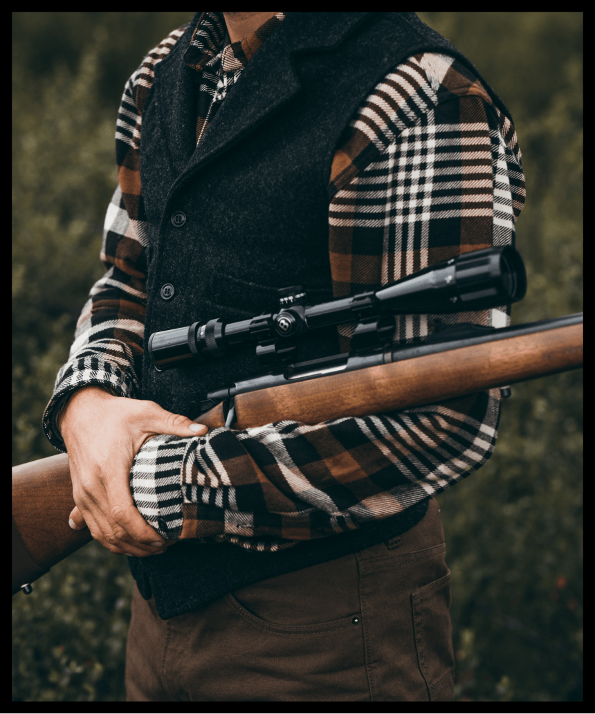 man in brown and white flannel holding hunting rifle with scope in grass field