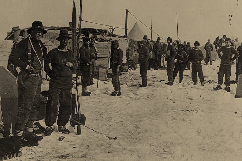 vintage black and white image of Men in black snow gear in a field with tents in a snowy field