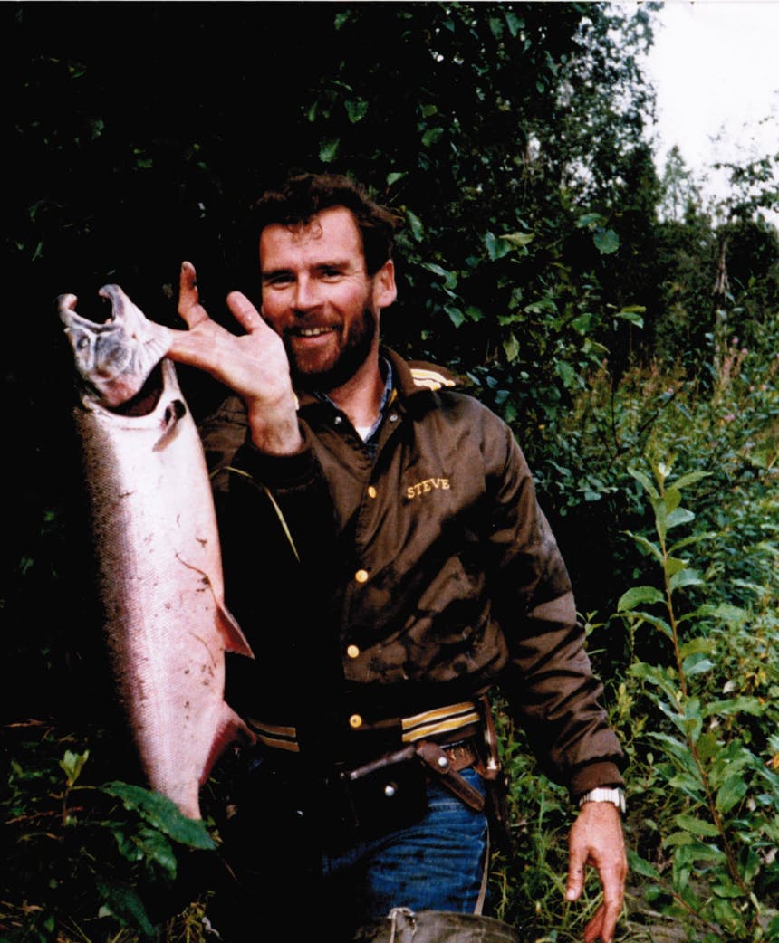 man in brown coat holding a large fish by it's gill slits