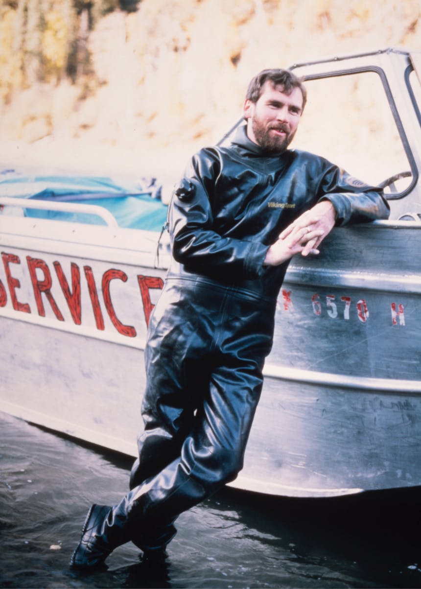 person in a full body diving suit leaning up next to an aluminum boat