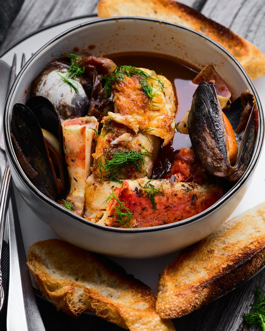 seafood stew with grilled bread in a white bowl on a wooden table