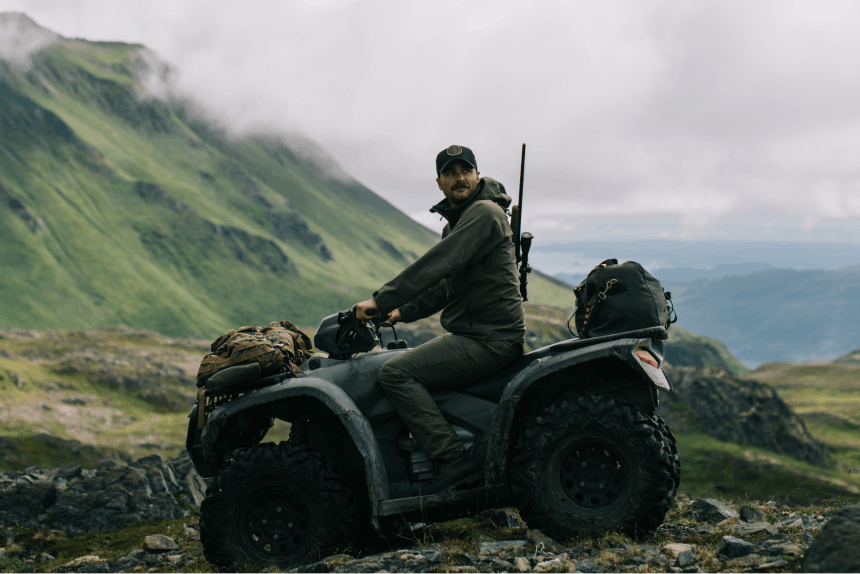 person on atv with rifle on his back in lush green mountain pass