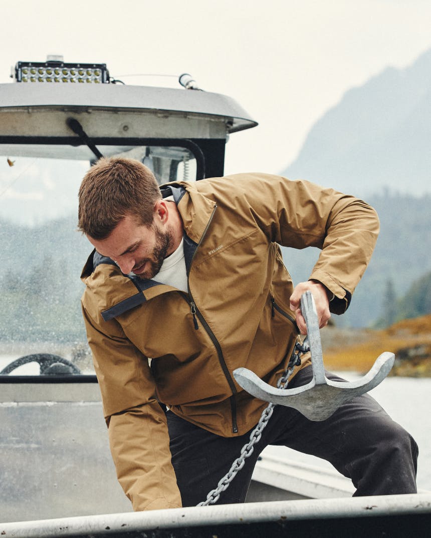 man in brown rain shell holding an anchor on a chain on a boat