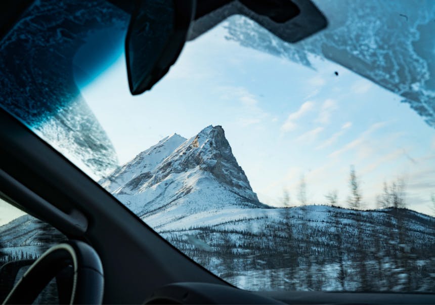 mountainous inselberg rising from a pine dotted hill taken from behind the windshield of a car