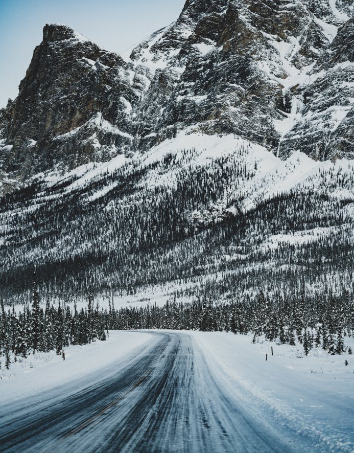 frozen road trailing away toward a craggy snow covered mountain peak