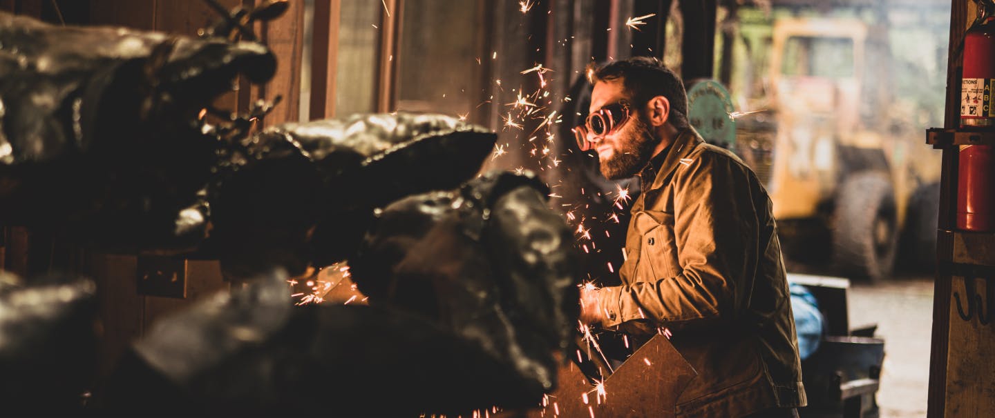 person in goggles making sparks while working on a metal sculpture in a workshop