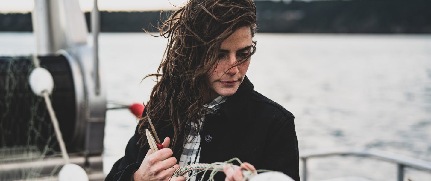 woman in black coat holding a floater on a fishing net while standing on a boat