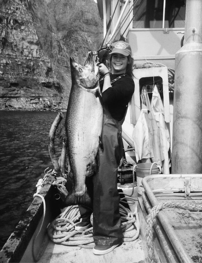 woman on boat near sheer rocky cliffs holding a gigantic fish while on the deck