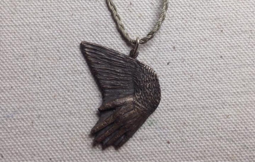 closeup detail of necklace pendant with stylized hand and wing formation on cord